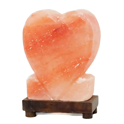 Upright heart-shaped Himalayan salt lamp with a timber base, glowing warmly in a cozy room.