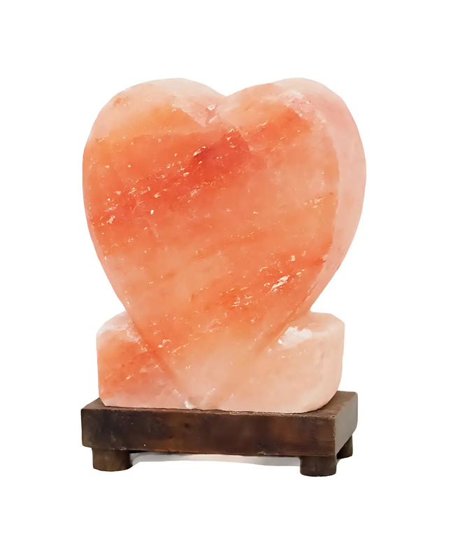 Upright heart-shaped Himalayan salt lamp with a timber base, glowing warmly in a cozy room.
