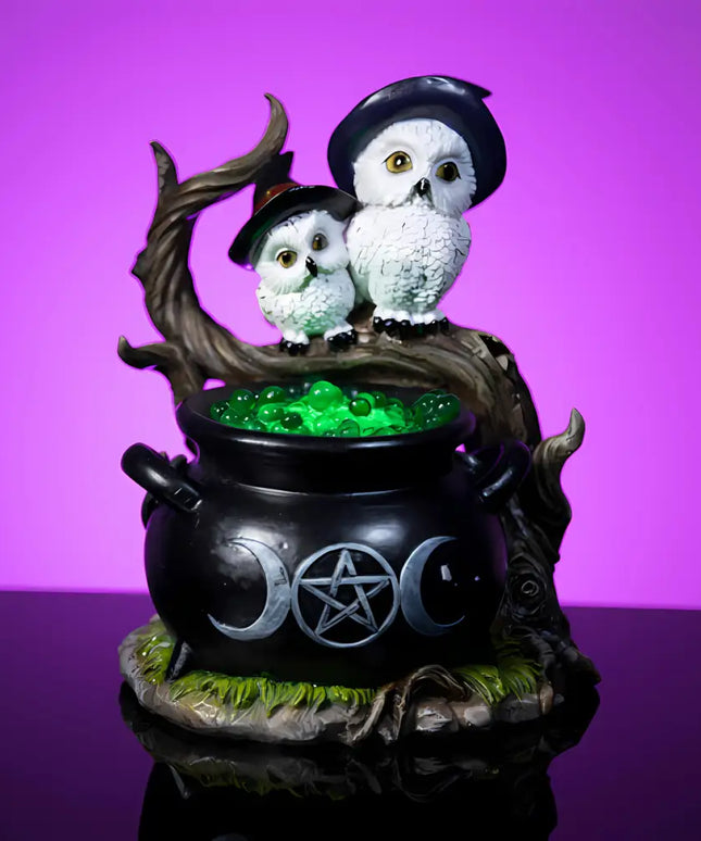 Two white owls wearing witches’ hats perched on a mystical cauldron
